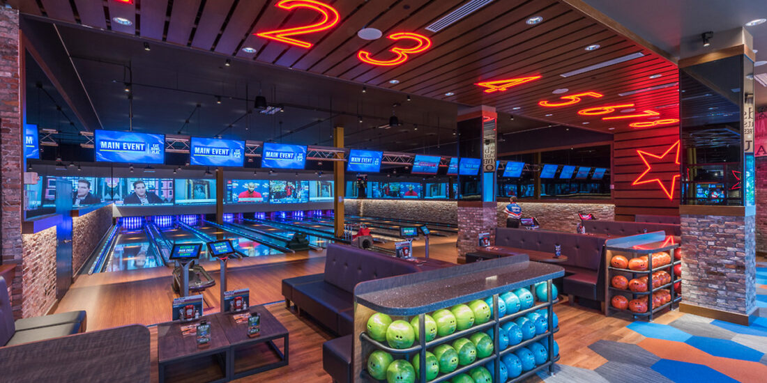 Bowling lanes at Main Event entertainment center, featuring modern seating, vibrant lighting, and large digital screens above each lane.
