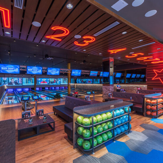 Bowling lanes at Main Event entertainment center, featuring modern seating, vibrant lighting, and large digital screens above each lane.