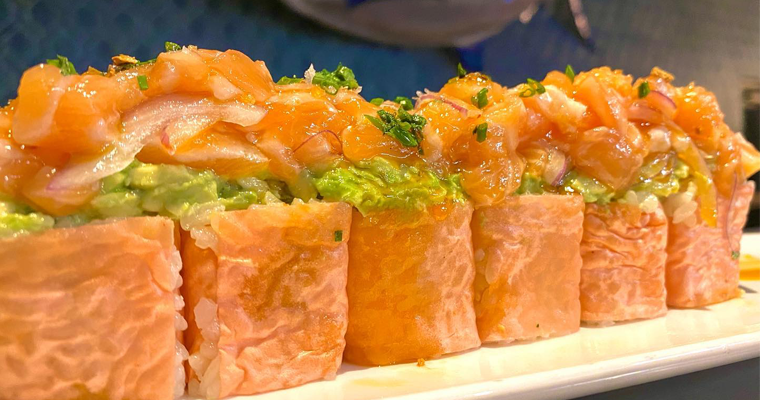 Close-up of a sushi platter featuring assorted fresh sushi rolls, garnished with vibrant green herbs and vegetables, presented on a dark, elegant serving dish.